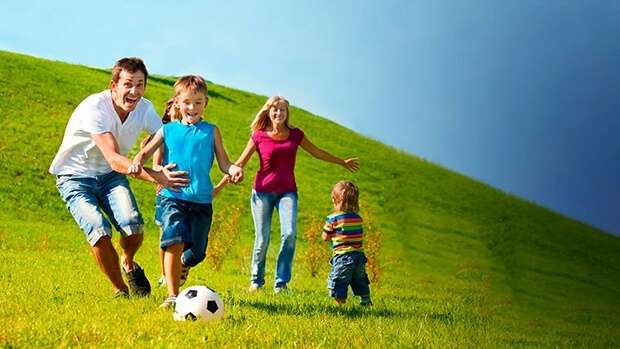 Family playing soccer outdoors on a hill.