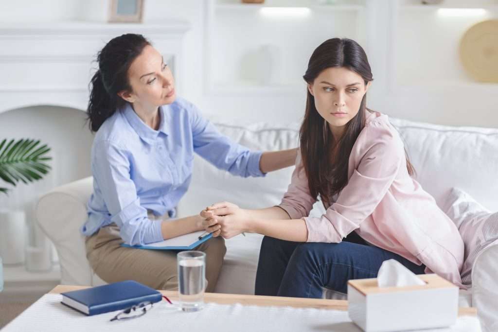 Therapist comforting sad patient on couch.